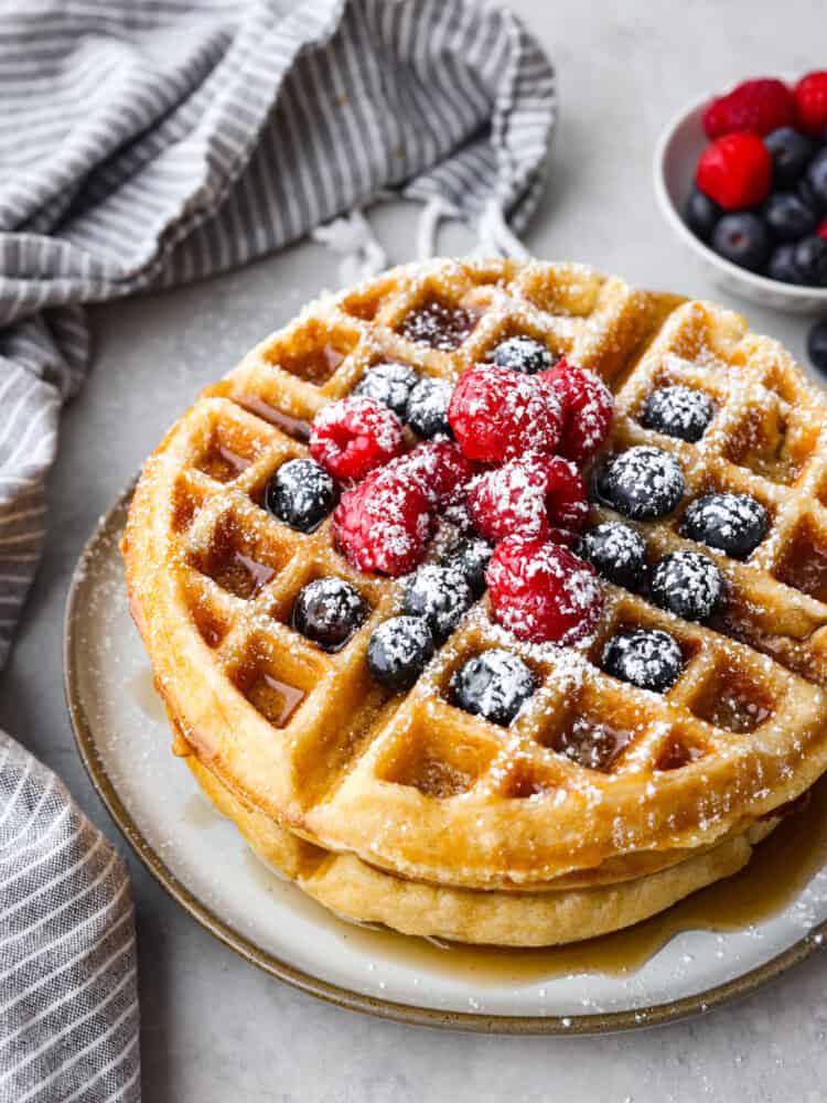 Buttermilk waffles are a classic breakfast recipe that is a family favorite! Fluffy and light on the inside with a crispy golden outside...buttermilk just makes everything better! A stack of 2 waffles on a gray stoneware plate, garnished with berries and powdered sugar.