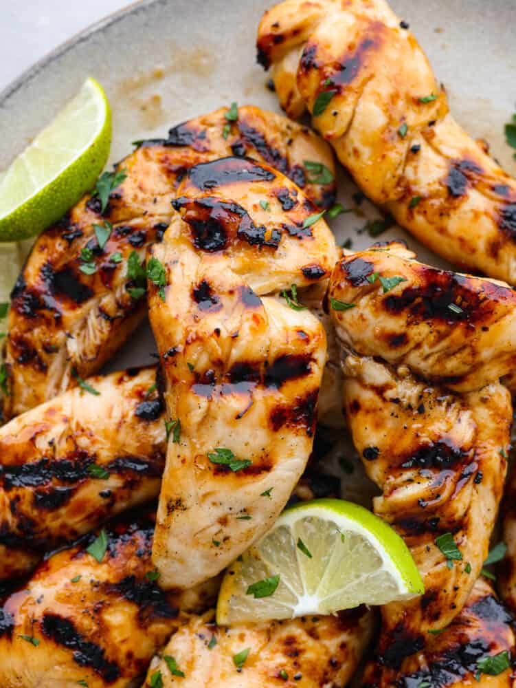 Juicy and flavorful, these 4-ingredient grilled chicken tenders are going to be your favorite thing to cook up this summer! They have a delicious honey lime glaze you'll be licking off your fingers! Closeup of chicken tenders garnished with chopped herbs and a lime slice.
