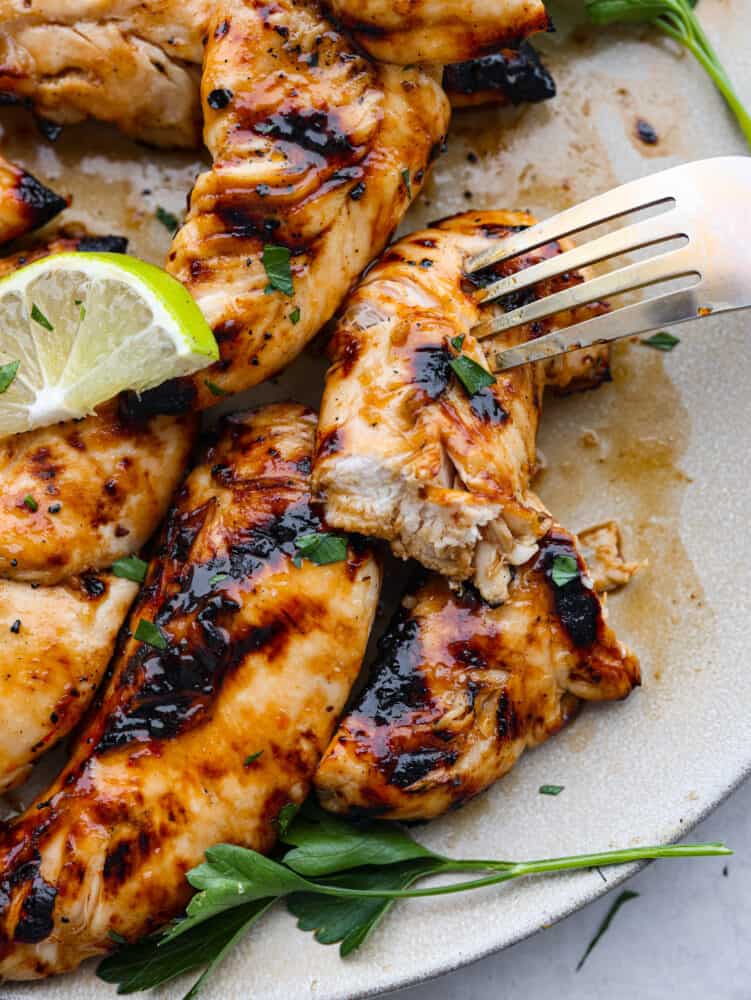 Juicy and flavorful, these 4-ingredient grilled chicken tenders are going to be your favorite thing to cook up this summer! They have a delicious honey lime glaze you'll be licking off your fingers! A cut chicken tender being skewered with a fork.