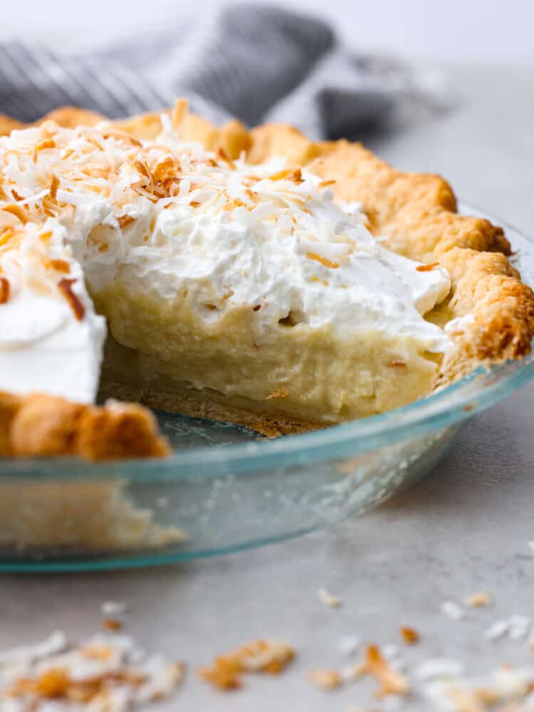 This Coconut Cream Pie recipe is made from scratch and well worth the effort! It's made with a creamy coconut custard filling and topped with sweetened whipped cream and toasted coconut. #pie #recipe #dessert #coconut The side view of coconut cream pie with a slice taken out of the pie pan.