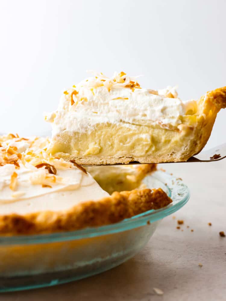 This Coconut Cream Pie recipe is made from scratch and well worth the effort! It's made with a creamy coconut custard filling and topped with sweetened whipped cream and toasted coconut. #pie #recipe #dessert #coconut A slice of coconut cream pie being served from a pie dish.