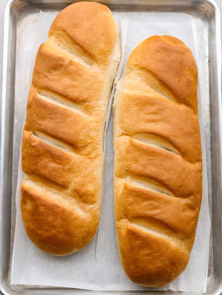 Making homemade French bread is a game-changer! Golden on the outside and supremely soft and tender on the inside, it will complement any meal perfectly! Top-down view of 2 French bread loaves on a baking sheet.