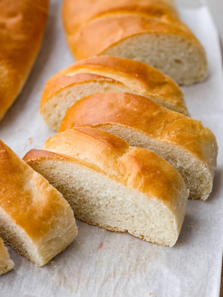 Making homemade French bread is a game-changer! Golden on the outside and supremely soft and tender on the inside, it will complement any meal perfectly! Sliced French bread on parchment paper.