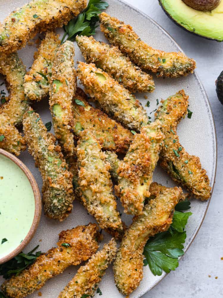 Insanely delicious and perfect for dipping, these fried avocado slices are the best appetizer choice! You're going to love their crispy, golden panko shell and buttery, creamy center. Closeup of fried avocado slices on a gray plate.