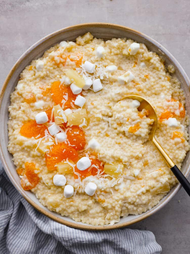 This delicious frog eye salad is creamy, fluffy, and filled with pineapple, mandarin oranges, and marshmallows. It is perfect for bringing to any gathering or potluck. Trust me when I say this will fly off the table! The top view of a frog eye salad with a golden serving spoon in it.