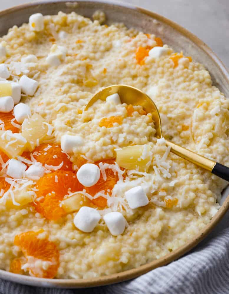 This delicious frog eye salad is creamy, fluffy, and filled with pineapple, mandarin oranges, and marshmallows. It is perfect for bringing to any gathering or potluck. Trust me when I say this will fly off the table! Frog eye salad ready to eat in a bowl with a gold serving spoon.