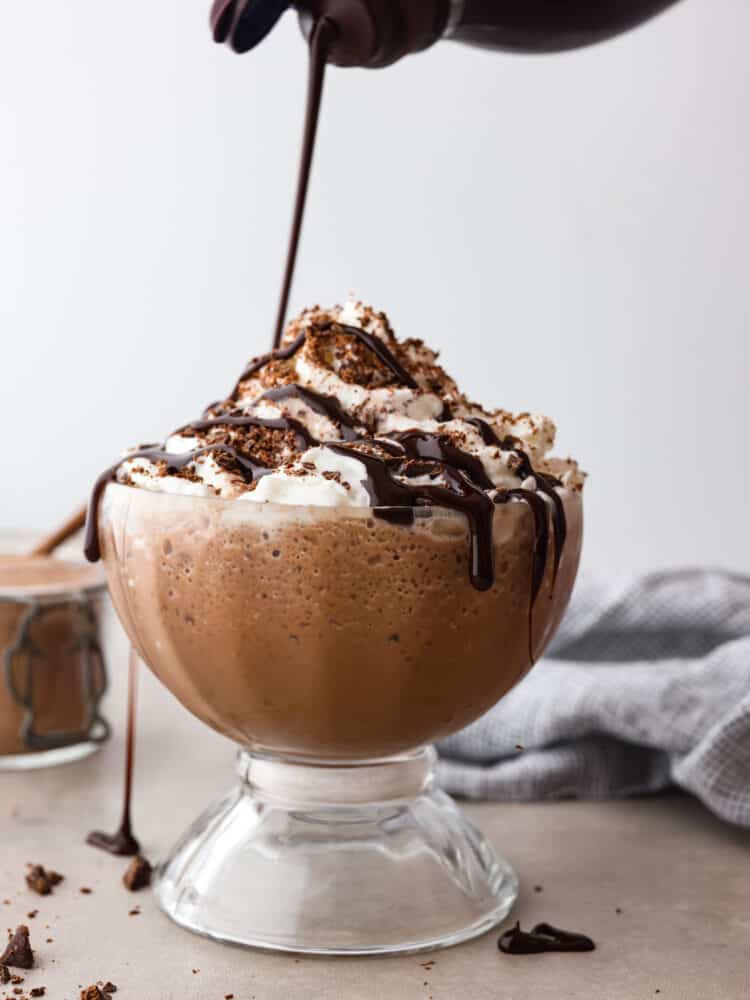 Craving hot chocolate in the summer? Now you can stay cool and satisfy your sweet tooth with a cup of this delicious frozen hot chocolate. It only takes a few simple ingredients to make and is ready in less than 5 minutes! Chocolate syrup being poured over a cup of frozen hot chocolate.