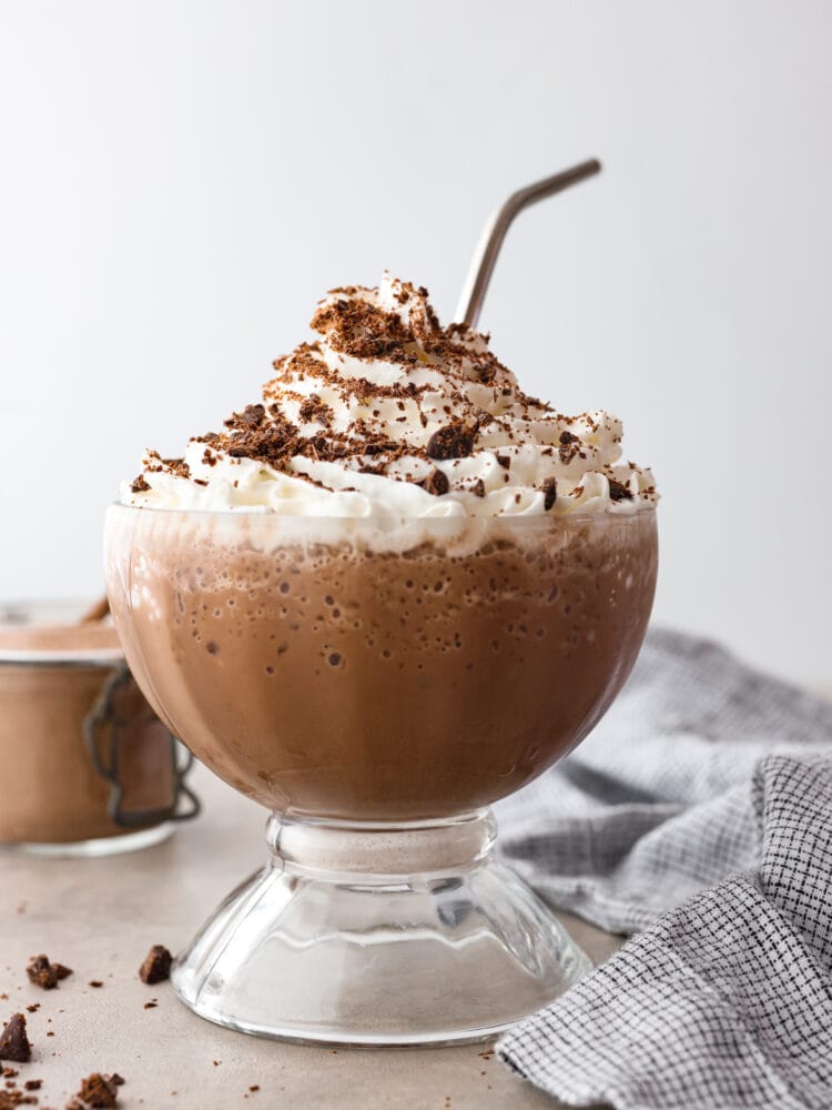 Craving hot chocolate in the summer? Now you can stay cool and satisfy your sweet tooth with a cup of this delicious frozen hot chocolate. It only takes a few simple ingredients to make and is ready in less than 5 minutes! Frozen hot chocolate in a glass cup, dusted with cocoa.