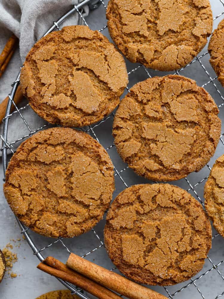 Crispy on the outside, warm and chewy on the inside, these Gingersnap Cookies are everything you want in a holiday dessert! They are the perfect way to finish off any holiday meal and leave everyone feeling merry and bright. Gingersnap cookies on a wire rack with cinnamon sticks.
