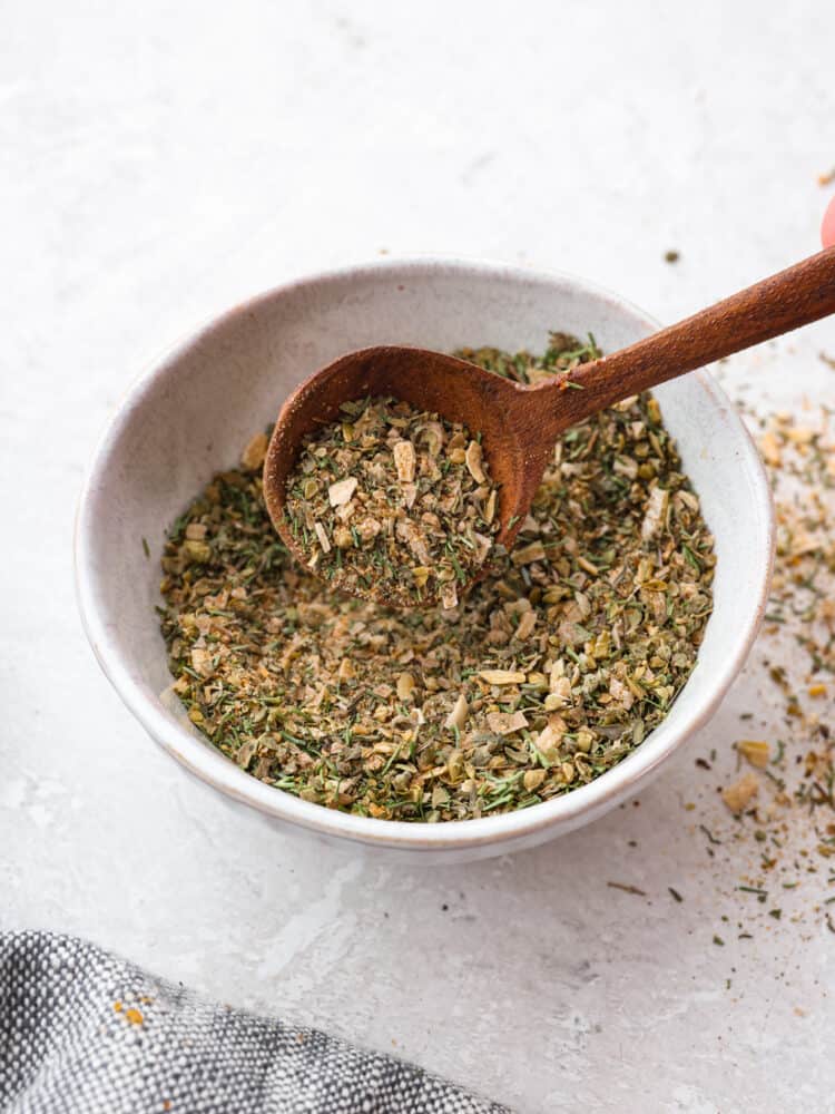 Using homemade Greek seasoning is the best way to add Mediterranean flair to your cooking! It mixes up in minutes and is perfect for adding delicious zesty flavor to all of your favorite meals. Scooping up Greek seasoning with a wooden spoon.