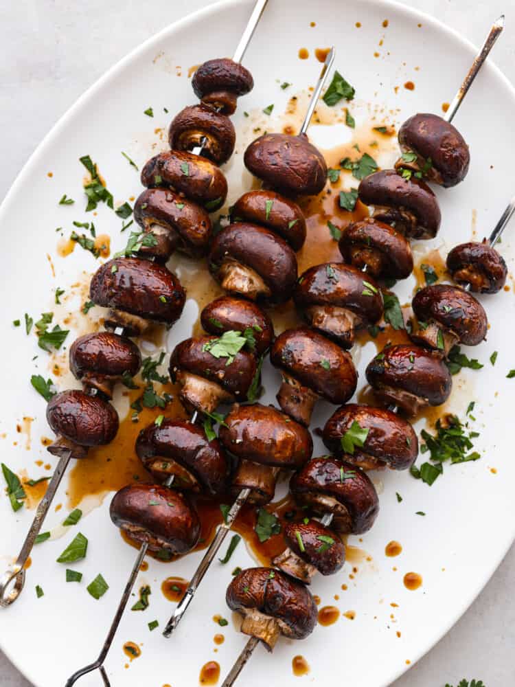 These vegan kabobs are the most delicious side dish that you MUST try! These grilled honey soy mushroom skewers are the perfect side dish for any entree, and you won't be able to stop at just one! A platter with mushroom skewers cooked and garnished.