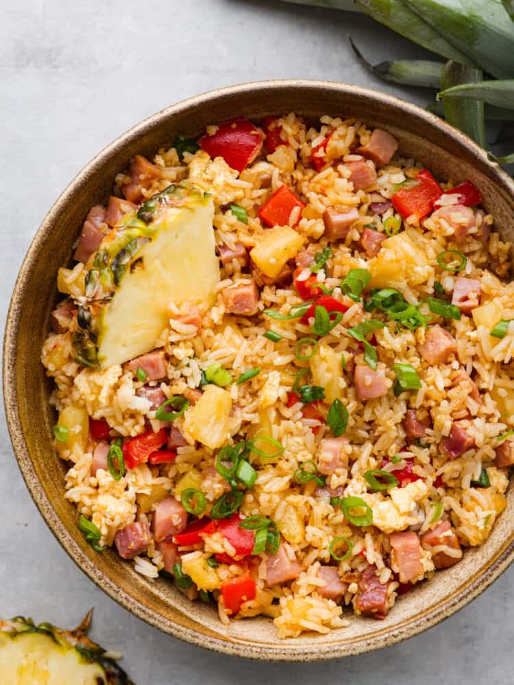 This Hawaiian fried rice is loaded with sweet pineapple, ham, and veggies and is so much better than takeout! Everyone goes crazy over this meal, and it's definitely a family favorite! Hawaiian fried rice in a brown bowl, ready to eat.