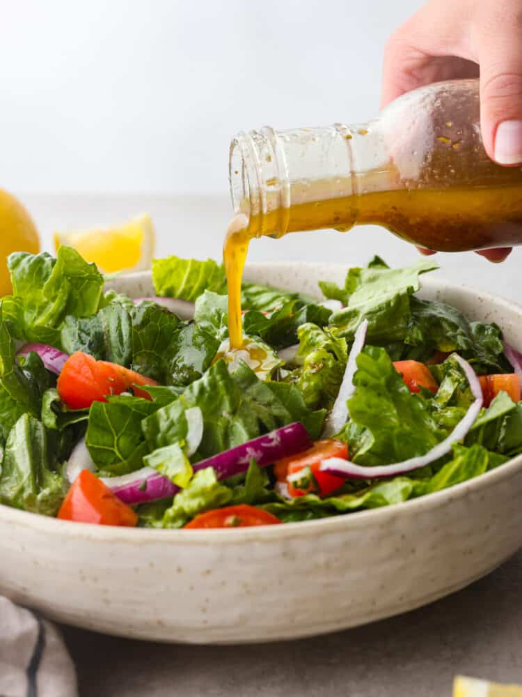 This homemade Italian dressing is the most delicious mixture of classic seasonings that will elevate any salad that you put it on. It has deep, complementing flavors that will leave your taste buds wanting more! Italian salad dressing being poured over a green salad.