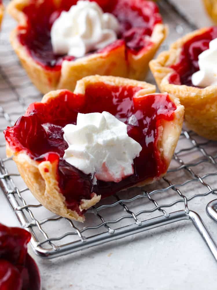 These mini cherry pies are perfect for any occasion! They have a flaky crust and a delightful cherry center that will definitely make you want to devour more than one! A mini cherry pie on a cooling rack that has a bite taken out of it.