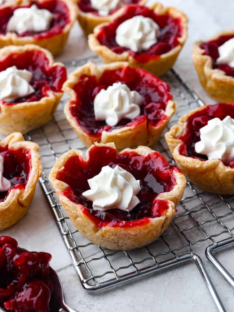 These mini cherry pies are perfect for any occasion! They have a flaky crust and a delightful cherry center that will definitely make you want to devour more than one! Mini cherry pies on a cooling rack.