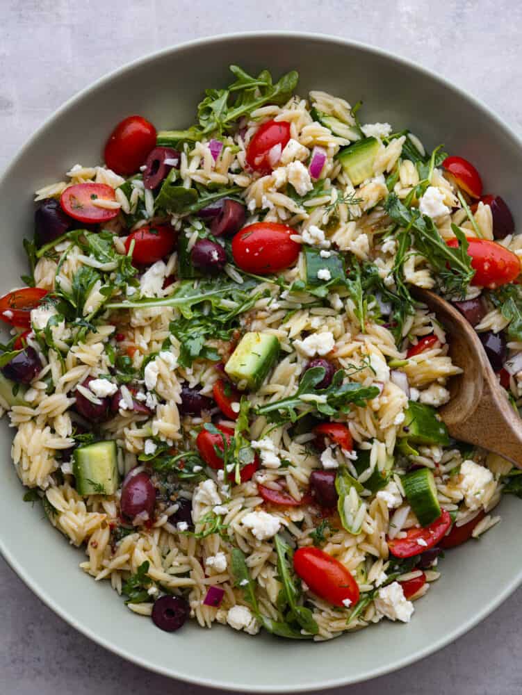 If you are looking for a delicious salad full of flavor and packed with different textures, then this Greek orzo salad is for you! Vegetables and arugula drizzled with a lemon vinaigrette combine to make the most delicious and refreshing taste! The top view of a bowl of Greek orzo salad.