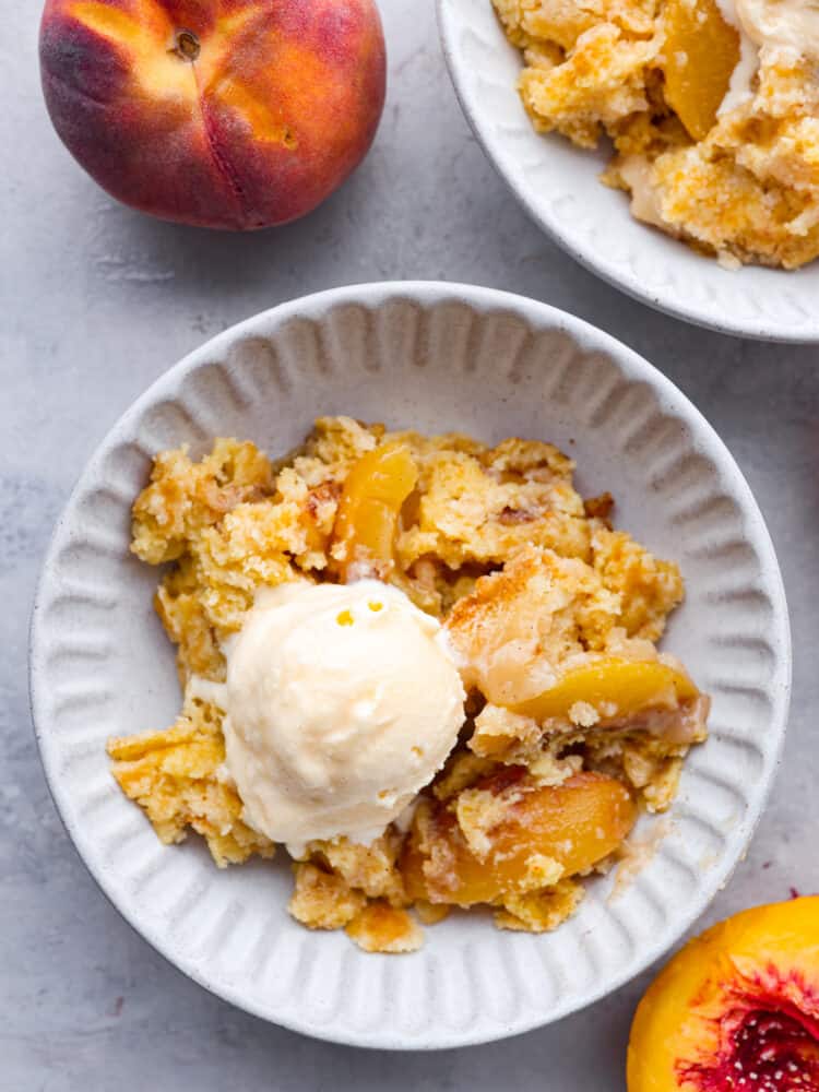 This 5-ingredient peach dump cake is a super easy dessert that is full of warm, cinnamony goodness. Top it off with a scoop of ice cream for a peachy, indulgent dessert the whole family will love. Top-down view of a scoop of peach dump cake in a white bowl served with ice cream.