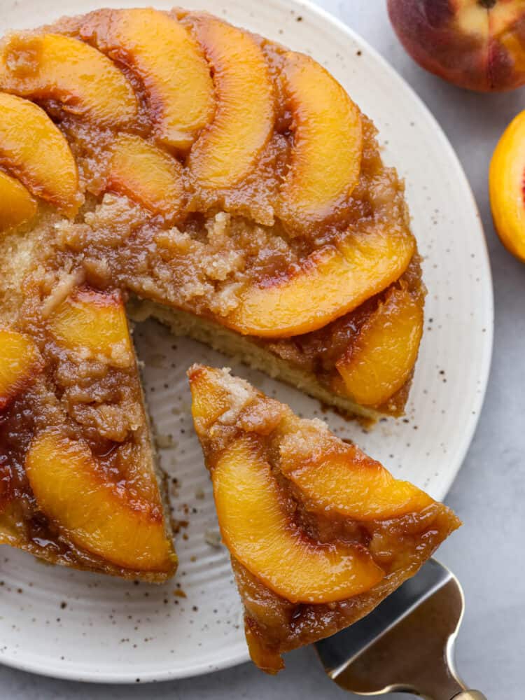 Get ready for your mouth to water as I tell you about this amazingly delicious peach upside-down cake! It is juicy, full of sweet flavor from brown sugar crumbles, and the best part... The soft, melt-in-your-mouth cake that combines it all together! A peach upside down cake with a slice being taken out.