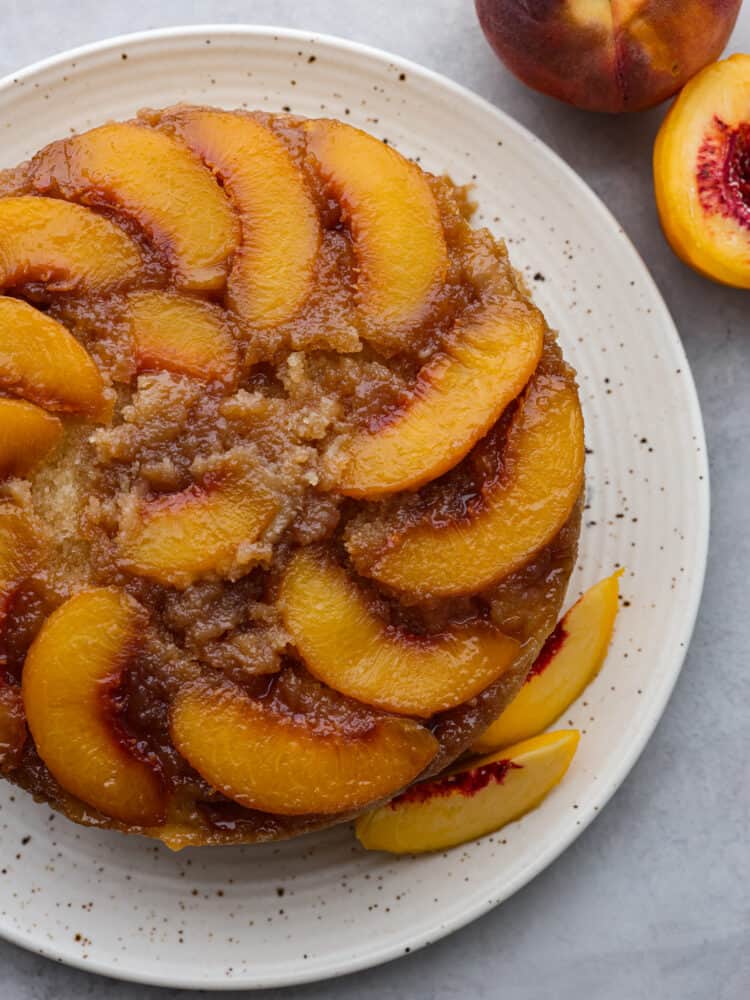 Get ready for your mouth to water as I tell you about this amazingly delicious peach upside-down cake! It is juicy, full of sweet flavor from brown sugar crumbles, and the best part... The soft, melt-in-your-mouth cake that combines it all together! A peach upside down cake on a white speckled platter.