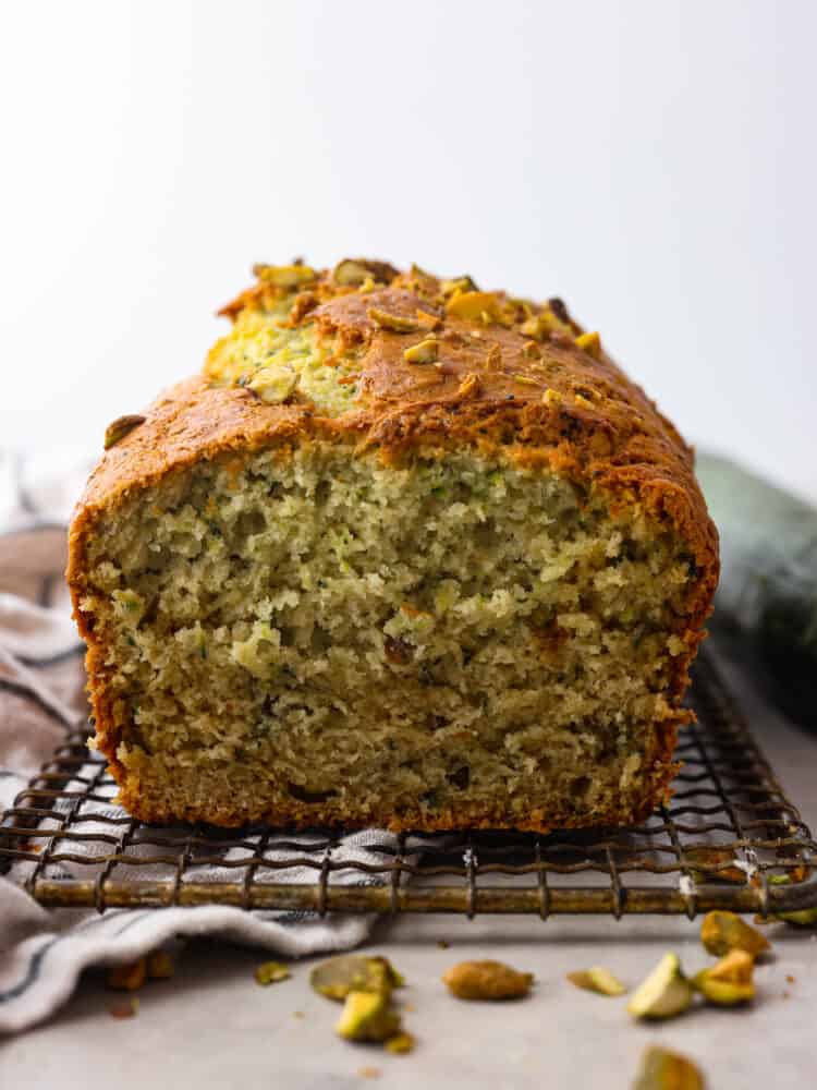 This deliciously soft pistachio zucchini bread is the perfect twist on a classic recipe. Packed with tons of unique flavor combinations from the pistachios and zucchini, you will LOVE this bread! The side view of a loaf of piztachio zucchini bread on a cooling rack with the end cut off.