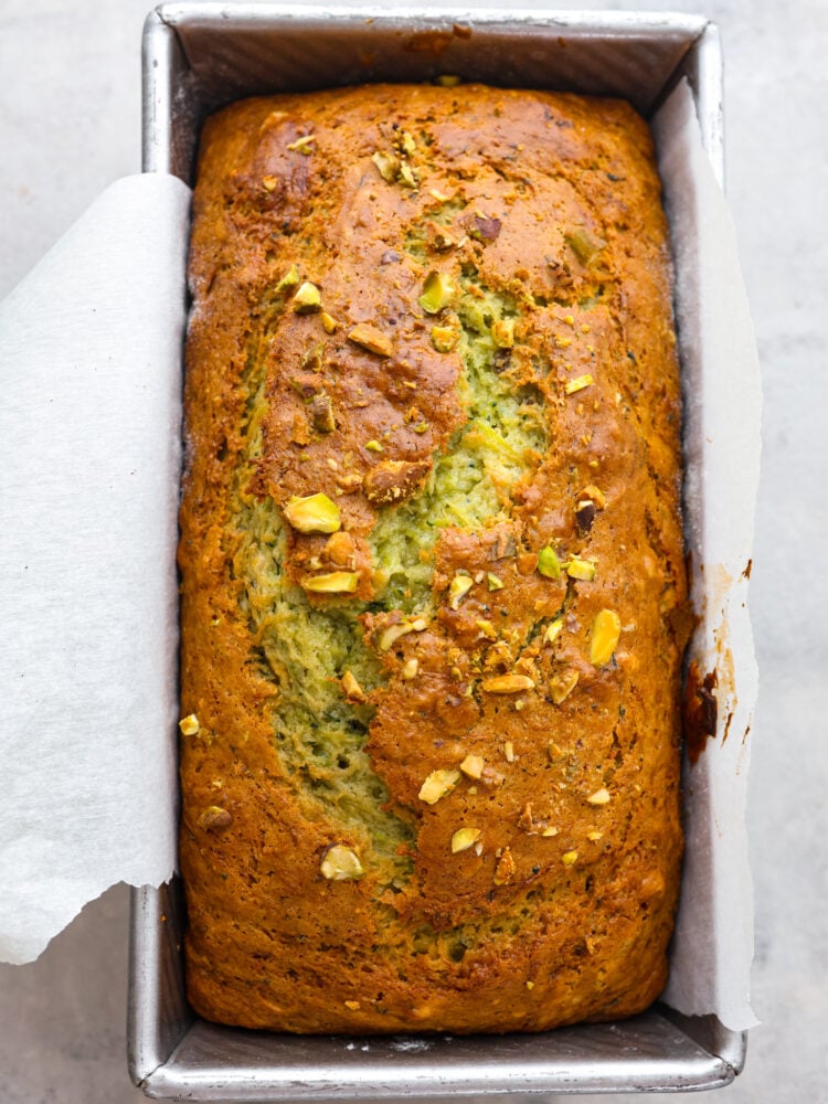This deliciously soft pistachio zucchini bread is the perfect twist on a classic recipe. Packed with tons of unique flavor combinations from the pistachios and zucchini, you will LOVE this bread! The top view of pistachio zucchini bread in a loaf pan, baked and ready to eat.