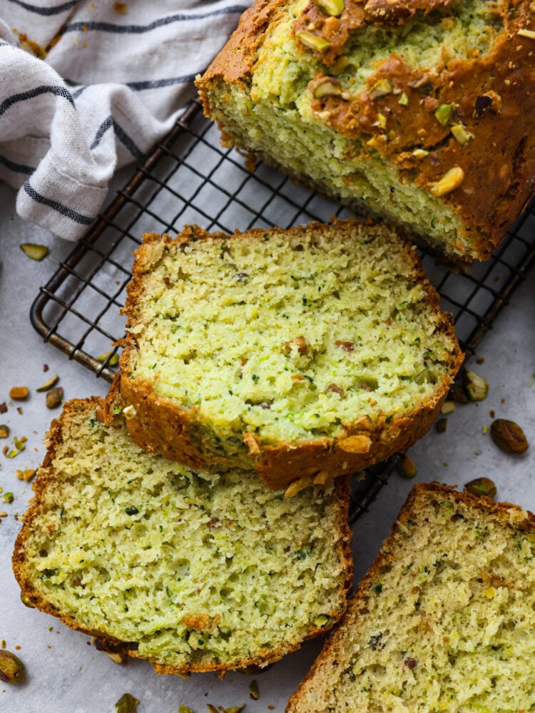 This deliciously soft pistachio zucchini bread is the perfect twist on a classic recipe. Packed with tons of unique flavor combinations from the pistachios and zucchini, you will LOVE this bread! A loaf of pistachio bread on a cooling rack with the end sliced.