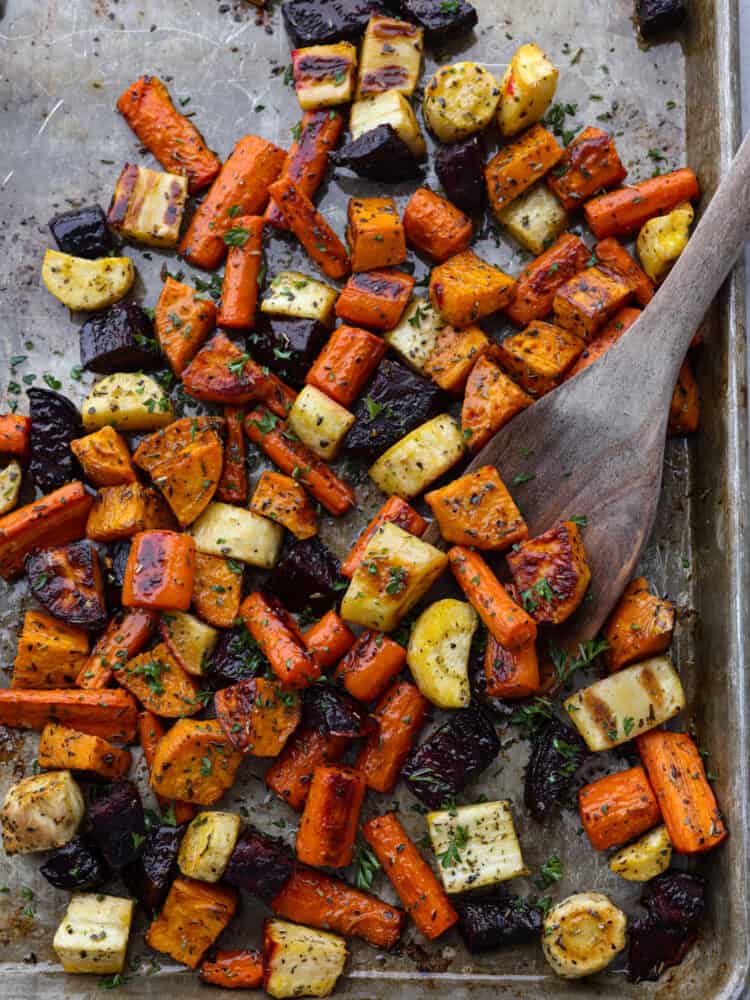 You have not had delicious vegetables until you have tried these roasted root vegetables! They have SO much flavor, and their texture is so tender that you will want to eat these with every meal! A baking sheet with roasted root vegetables being scooped up with a wooden spoon.