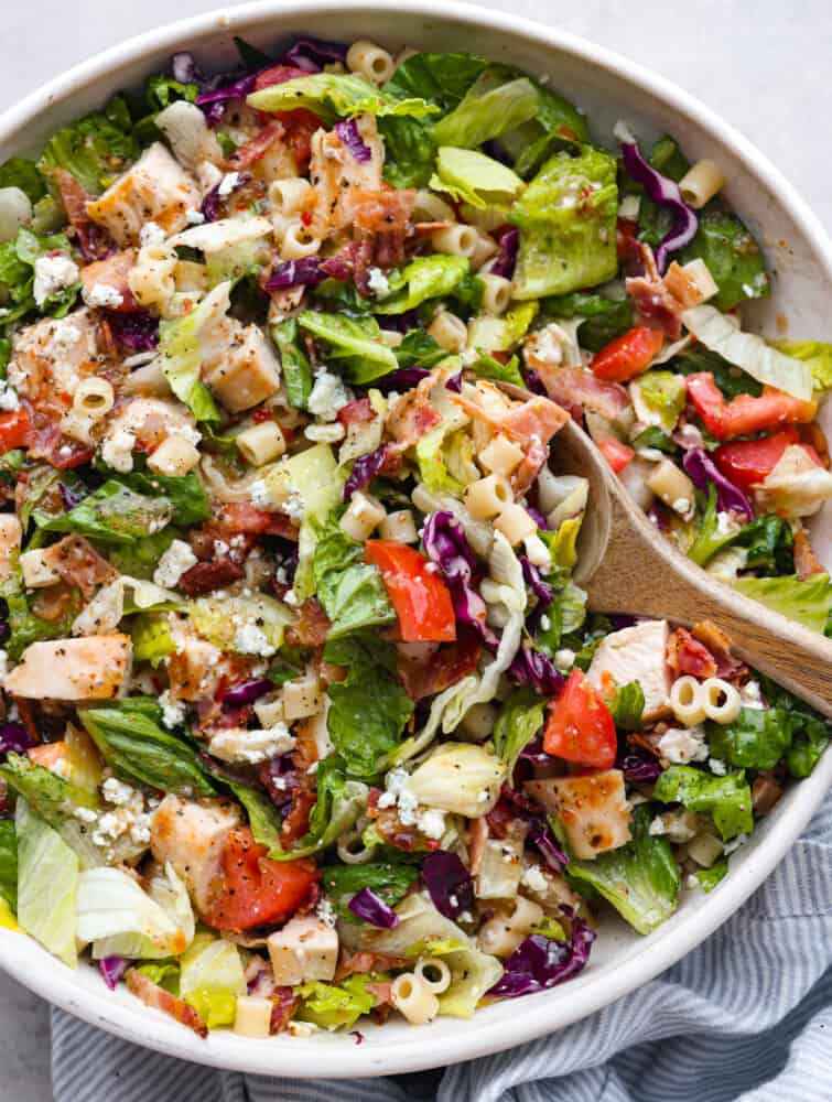 This copycat portillo's chopped salad is the best combination of all time! Romaine lettuce seasoned with a delicious and flavorful vinaigrette dressing. Topped with some pasta, veggies, and cheese, you can't forget the best part... the bacon! The top view of a Portillo's chopped salad with a wooden spoon.