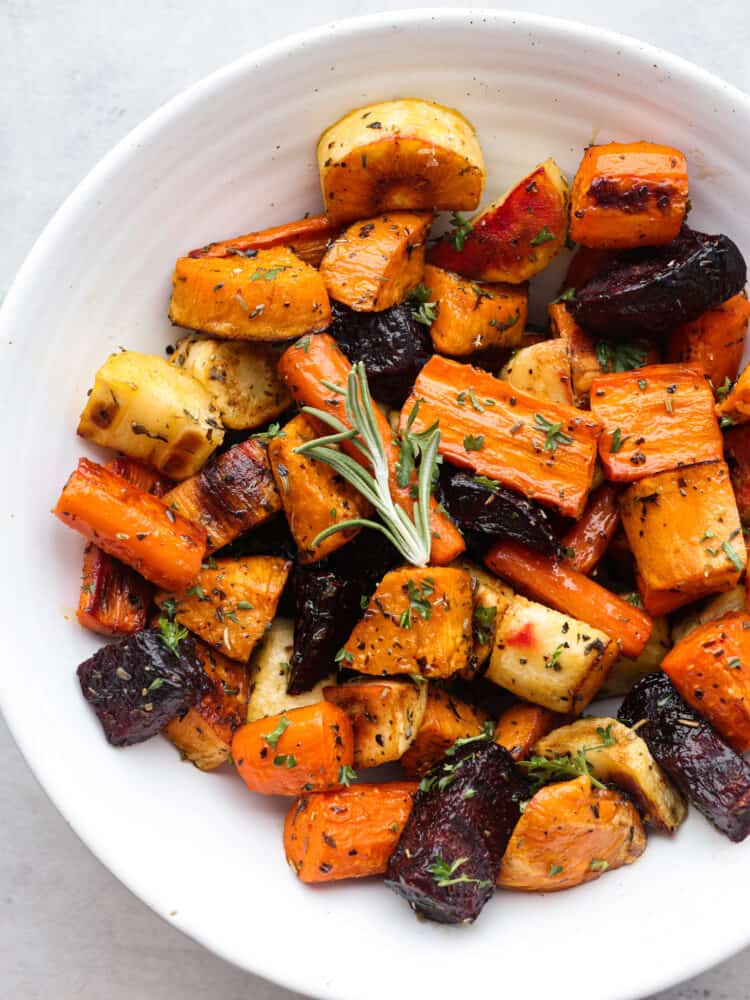 You have not had delicious vegetables until you have tried these roasted root vegetables! They have SO much flavor, and their texture is so tender that you will want to eat these with every meal! A white bowl filled with roasted root vegetables.