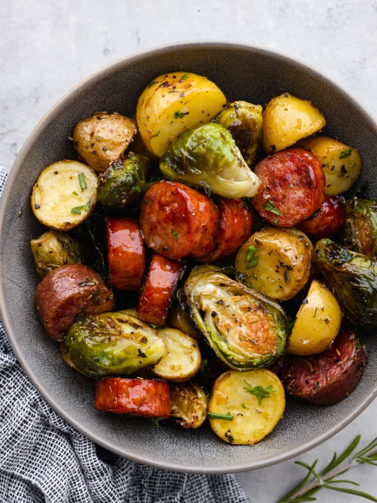 This sheet pan sausage and veggies are straight from heaven! This recipe has potatoes, sausage, and Brussel sprouts that are all perfectly seasoned with dried Italian herbs. You will want to eat every last bite! Sausage, Brussel sprouts and potatoes all cooked and seasoned and in a gray bowl.