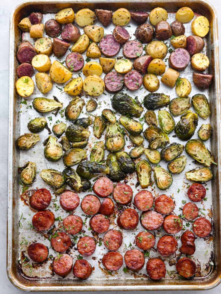 This sheet pan sausage and veggies are straight from heaven! This recipe has potatoes, sausage, and Brussel sprouts that are all perfectly seasoned with dried Italian herbs. You will want to eat every last bite! A sheet pan with cooked sausage and veggies on it.