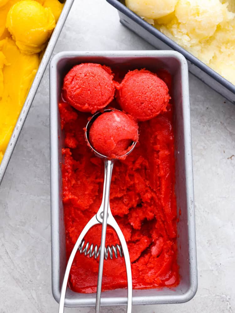 Get ready for the most refreshing homemade sorbet that you have ever had with this perfect recipe! Silky smooth, packed full of flavor, and a delightful dessert for any occasion, this will knock your socks off! The top vew of strawberry sorbet in a bread pan with a scoop scooping out the sorbet.