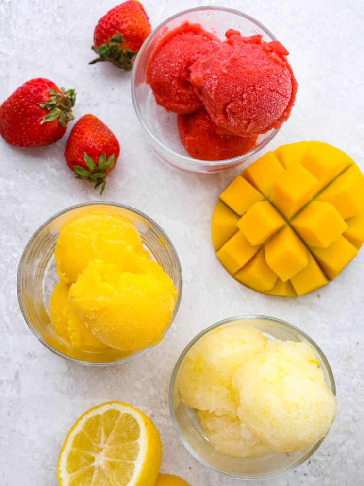 Get ready for the most refreshing homemade sorbet that you have ever had with this perfect recipe! Silky smooth, packed full of flavor, and a delightful dessert for any occasion, this will knock your socks off! The topview of strawberry sorbet, lemon sorbet and mango sorbet scooped in glass cups.