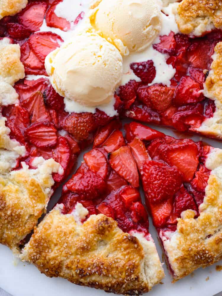 This fresh strawberry galette uses sweetened strawberries that are wrapped in a beautiful rustic buttery pastry and baked to perfection. Strawberry galette is a much easier version of a pie, and it will become your new favorite strawberry dessert! A closeup view of two slices cut out of the whole strawberry galette. Two scoops of ice cream are on top of the galette and starting to melt.