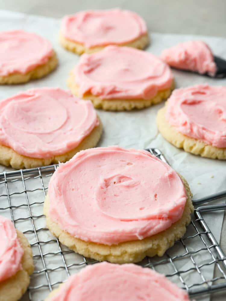 Look no more; this is the best copycat recipe out there for the famous Swig sugar cookie! These Swig sugar cookies are perfectly soft and topped with the most delightfully sweet frosting that you will ever try. You will definitely not be able to stop at just one! Sugar cookies with pink frosting on parchment paper and a cooling rack.