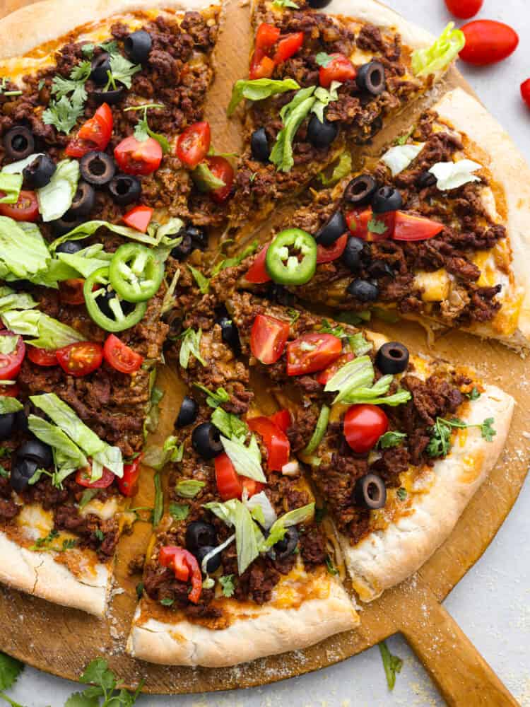 Two classic family favorites, pizza and tacos, come together in this easy weeknight meal that is destined to become a favorite in your home. Taco pizza is loaded with tasty seasoned beef, melty cheese, beans, and fresh veggies for a flavor combination you'll love! Sliced taco pizza on a wooden serving board.