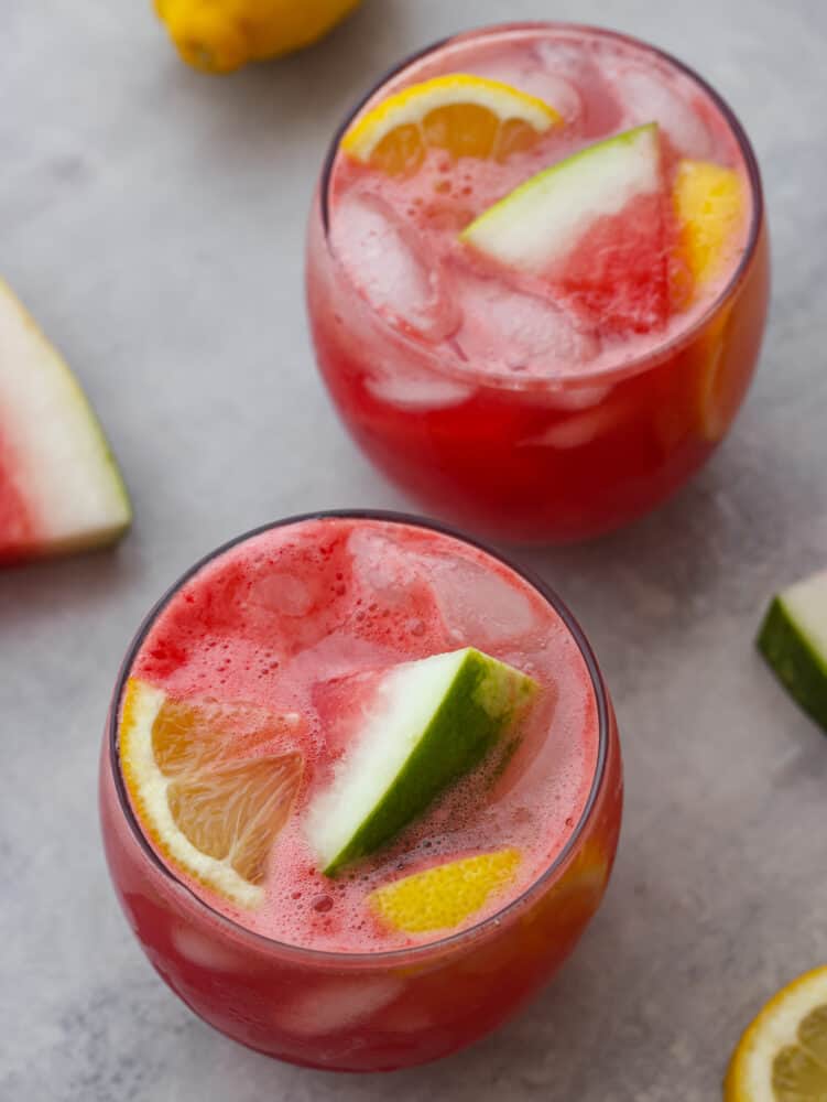 Juicy, sweet, and just a little bit sour, this sparkling watermelon lemonade is the most refreshing summer drink. Serve it at your next get-together and I promise it will be a huge hit! Top-down view of 2 cups of watermelon lemonade, garnished with lemon and watermelon slices.