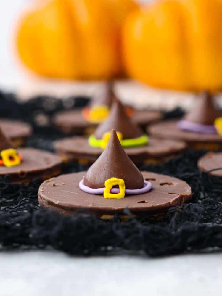 These Easy Witch Hat Cookies are sure to put a spell on your Halloween party guests! With a fudge cookie base and a Hershey's kiss on top, they are simple to put together and delicious to eat. These are the perfect treat for kids to help assemble and clean-up is a breeze. Closeup of a witch hat made with a chocolate cookie and Hershey's Kiss.