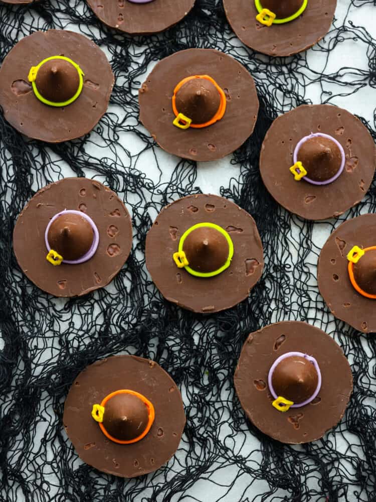 These Easy Witch Hat Cookies are sure to put a spell on your Halloween party guests! With a fudge cookie base and a Hershey's kiss on top, they are simple to put together and delicious to eat. These are the perfect treat for kids to help assemble and clean-up is a breeze. Top-down view of witch hat cookies on top of black netting.