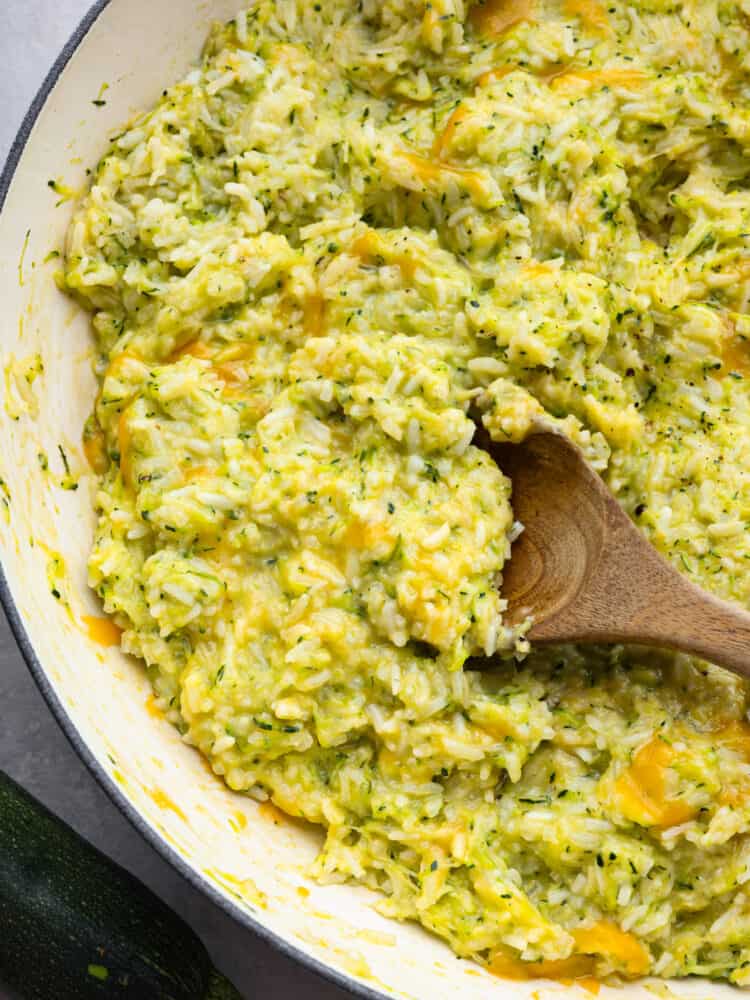 This Cheesy Zucchini Rice makes the best side to any meal. It is so cheesy and delicious and the best part is that it is hidden with zucchini! This will become a family favorite! A pan with cheesy zucchini rice with a wooden spoon.
