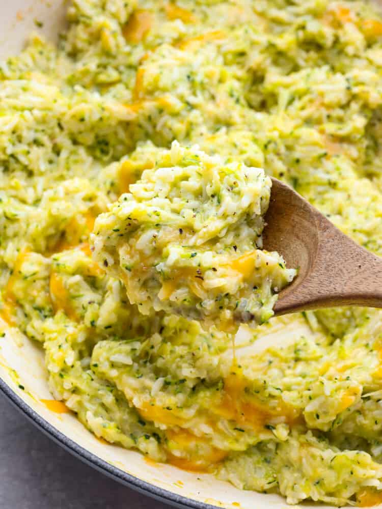 This cheesy zucchini rice is ooey gooey and a divine comfort food that makes the best side to any meal. It is so cheesy and delicious, and the best part is that it has a vegetable in it that my kids will actually eat! A close up of rice being served on a wooden spoon.