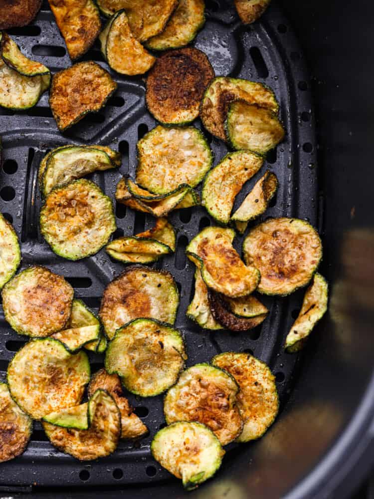If you're looking for a healthy and delicious way to use up your summer zucchini, making chips in the air fryer is the answer! They're low-carb, seasoned to perfection, and perfectly golden and crispy! Cooked zucchini chips in the bottom of an air fryer basket.