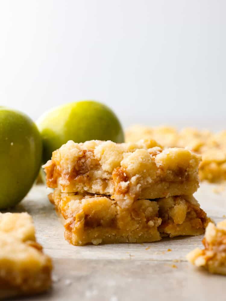 Salted caramel apple bars are ooey-gooey treats that have an amazing buttery shortbread crust and a soft and sweet caramel apple center!ย This is one of the best desserts you will make this fall! A stack of 2 salted caramel apple bars.