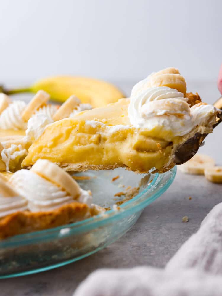 A classic dessert, made with a creamy vanilla bean and banana custard filling! This banana cream pie recipe is foolproof and ready to please a crowd! Picking up a slice of pie with a cake spatula.