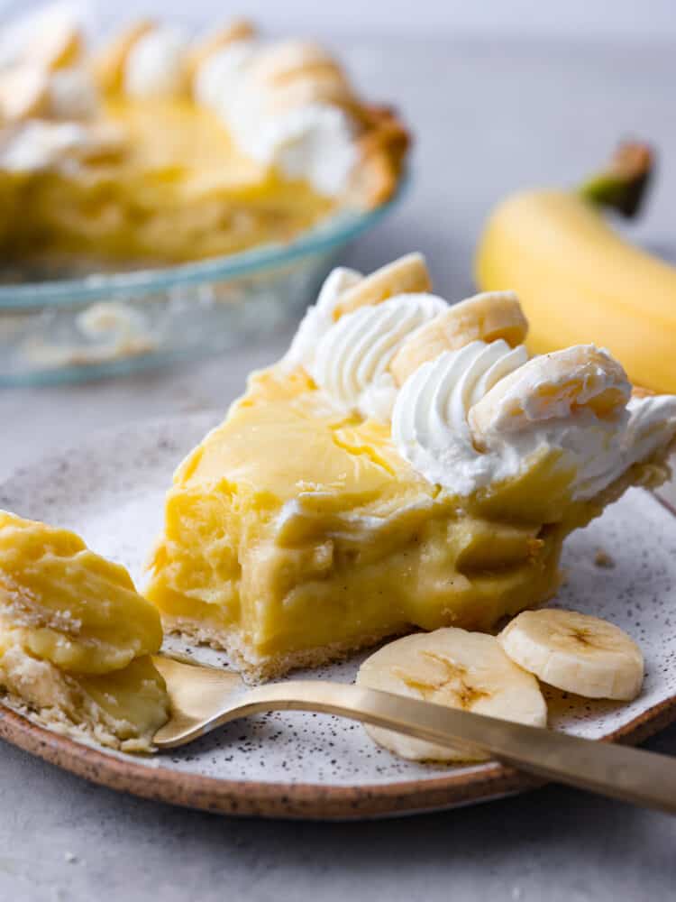 A classic dessert, made with a creamy vanilla bean and banana custard filling! This banana cream pie recipe is foolproof and ready to please a crowd! Closeup of a banana cream pie slice with a bite taken out of it.