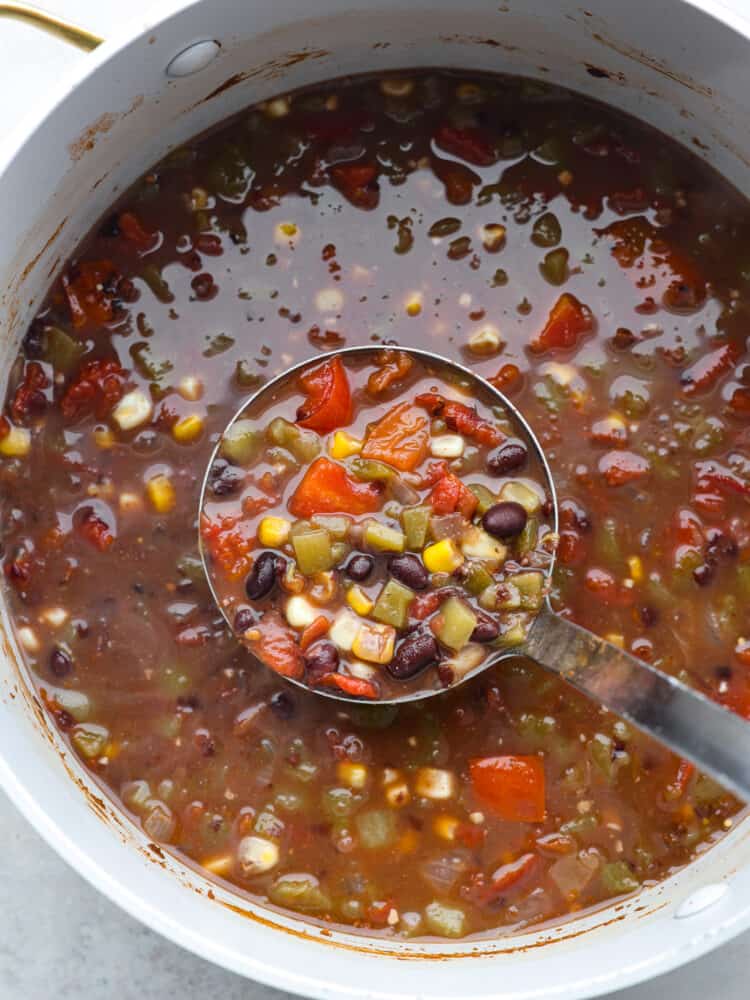 A super easy 20-minute black bean soup! This soup is hearty and filling and a great option for those wanting a vegetarian option! It's made with black beans, a variety of veggies, and delicious seasonings for a savory soup with a hint of warm spice! Black bean soup being served out of a large pot with a ladle.