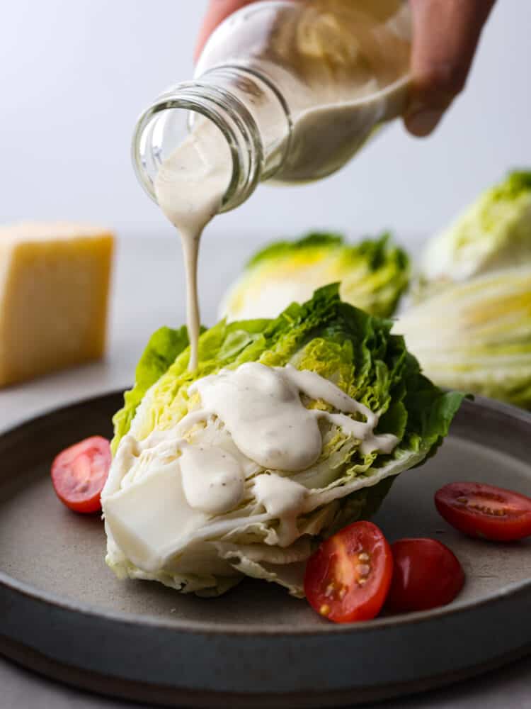 This caesar wedge salad is a twist on a classic starter and it's filled with delicious and fresh flavors! It's perfect for serving with every meal and your whole family will love it! Salad dressing being poured onto a wedge of lettuce.