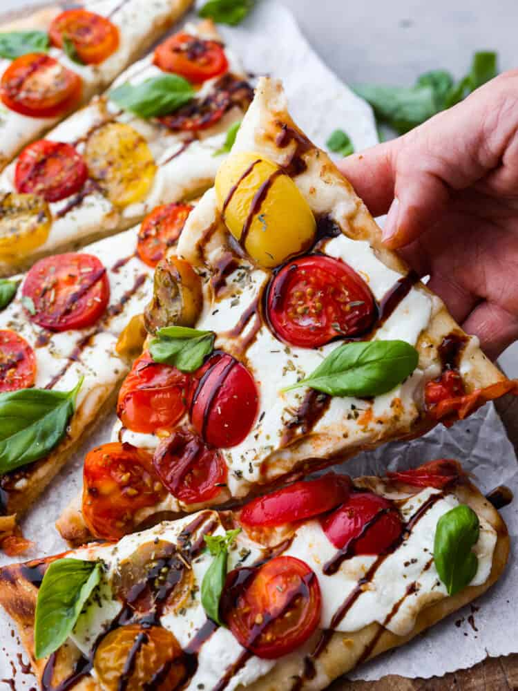 Light and fresh, this caprese flatbread is the perfect appetizer for any Italian-inspired meal! It’s topped with melty mozzarella, fresh herbs and veggies, and topped off with a mouthwatering balsamic glaze! Closeup of a slice of caprese flatbread.