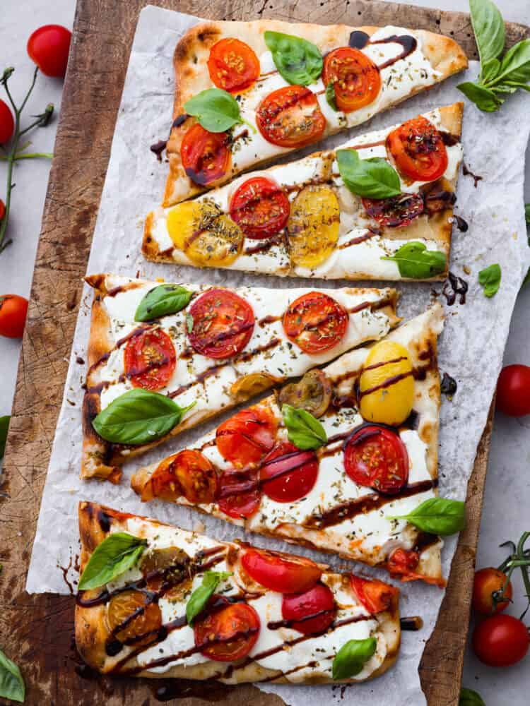 Light and fresh, this caprese flatbread is the perfect appetizer for any Italian-inspired meal! It’s topped with melty mozzarella, fresh herbs and veggies, and topped off with a mouthwatering balsamic glaze! Top-down view of sliced caprese flatbread on parchment paper.