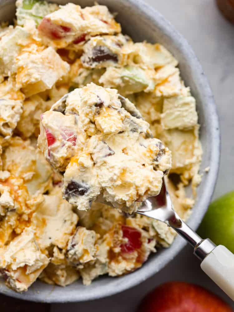Snickers salad is perfect for any potluck! It's a mixture of snickers bites and apples, all covered in a vanilla cool whip and topped with chocolate and caramel sauce. This perfectly sweet and salty salad is so delicious and surprisingly easy to make! A closeup of snickers apple salad on a spoon.